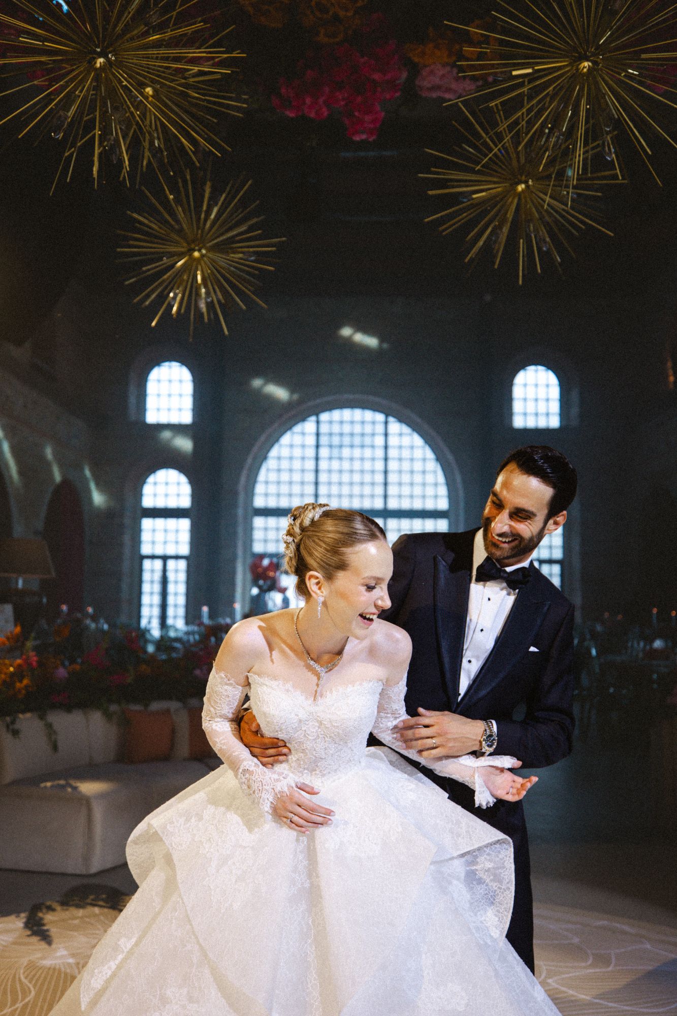 Bride and groom laughing under gold starburst chandeliers