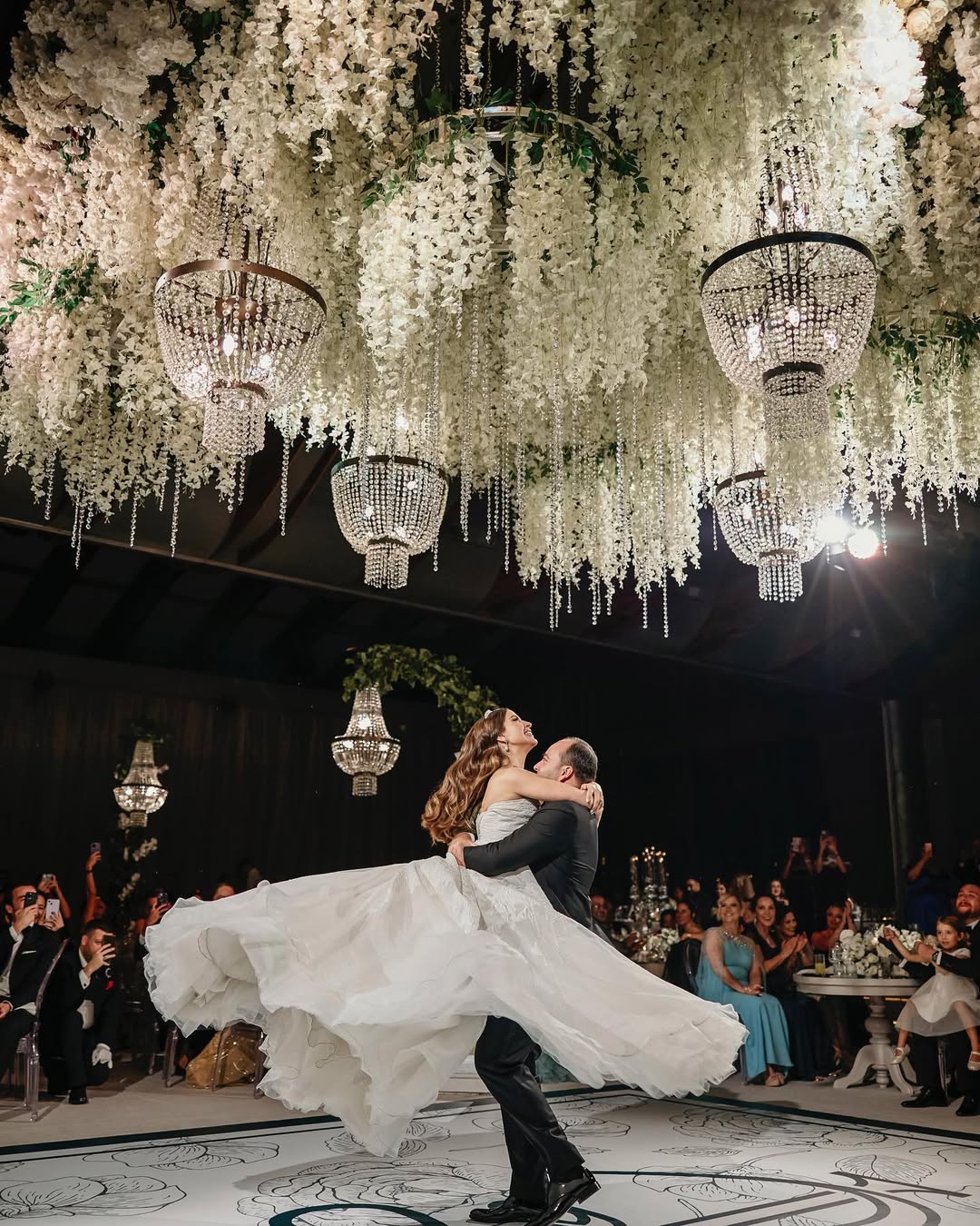 Bride lifted mid-dance beneath a white wisteria chandelier installation